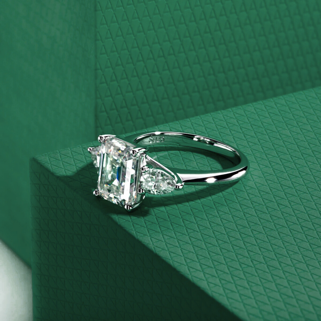 anel solitário prata 925 com lapidação esmeralda e pedras moissanite sobre fundo verde texturizado