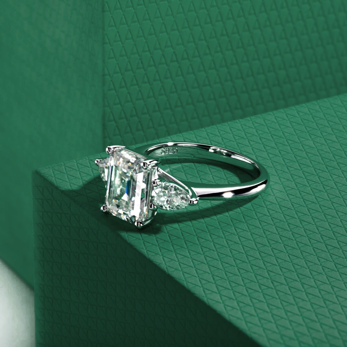 anel solitário prata 925 com lapidação esmeralda e pedras moissanite sobre fundo verde texturizado