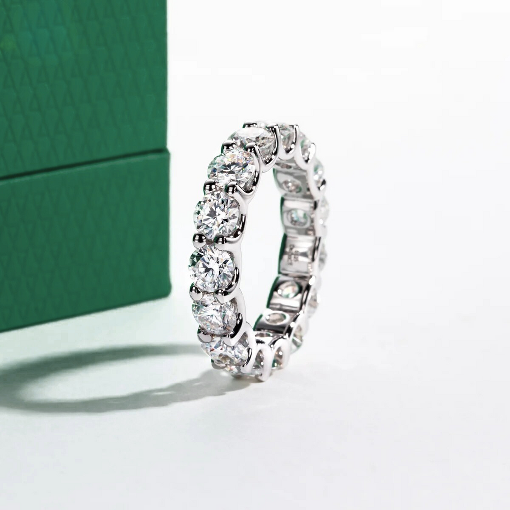 Aliança de prata com brilhantes moissanite redondos, ao lado de caixa verde texturizada