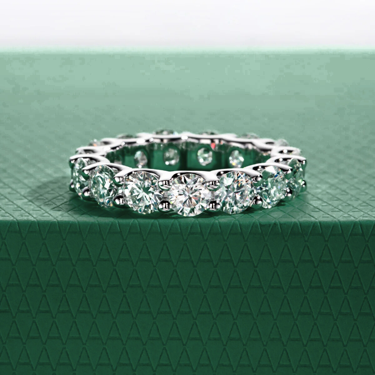 Aliança de moissanites brilhantes cravejada em metal prateado sobre fundo verde texturizado