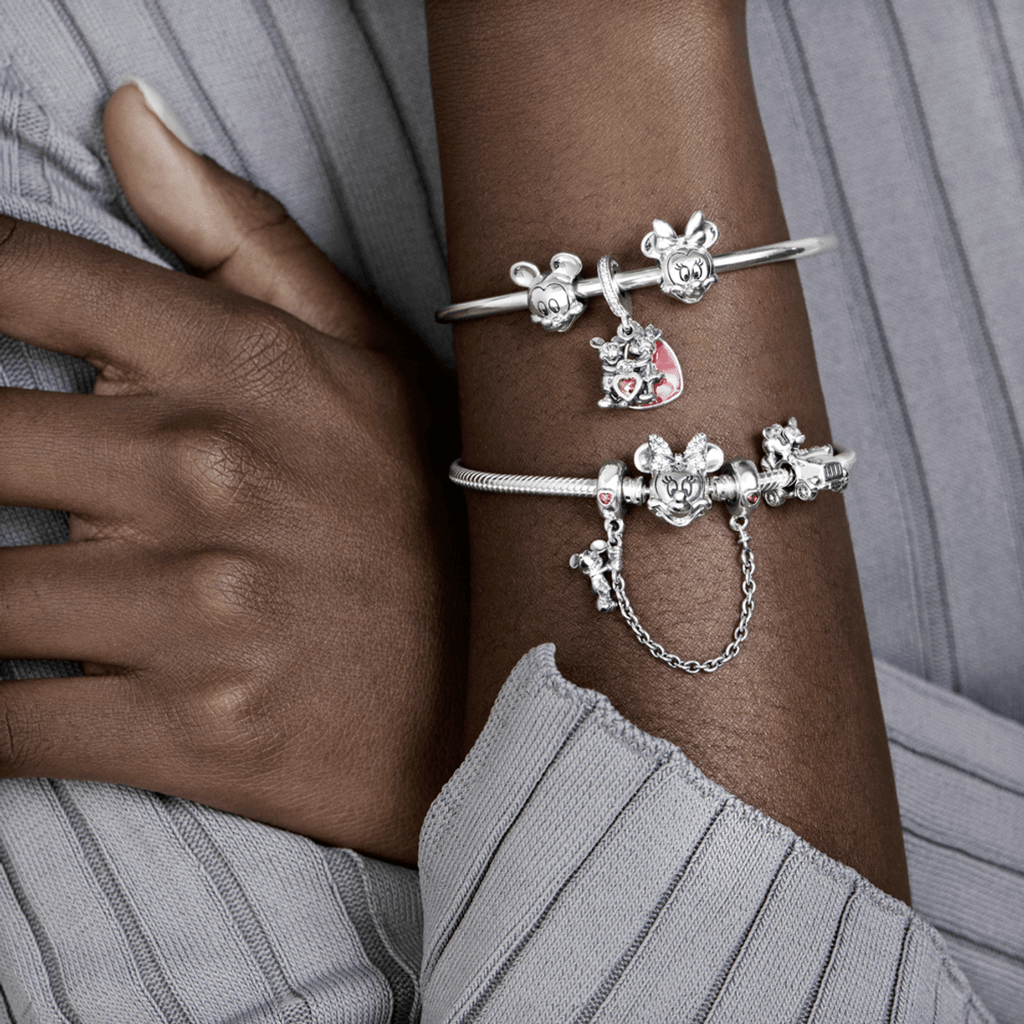 Pulseiras Pandora prateadas com charms de Minnie e Mickey Mouse no braço de pessoa negra com suéter cinza