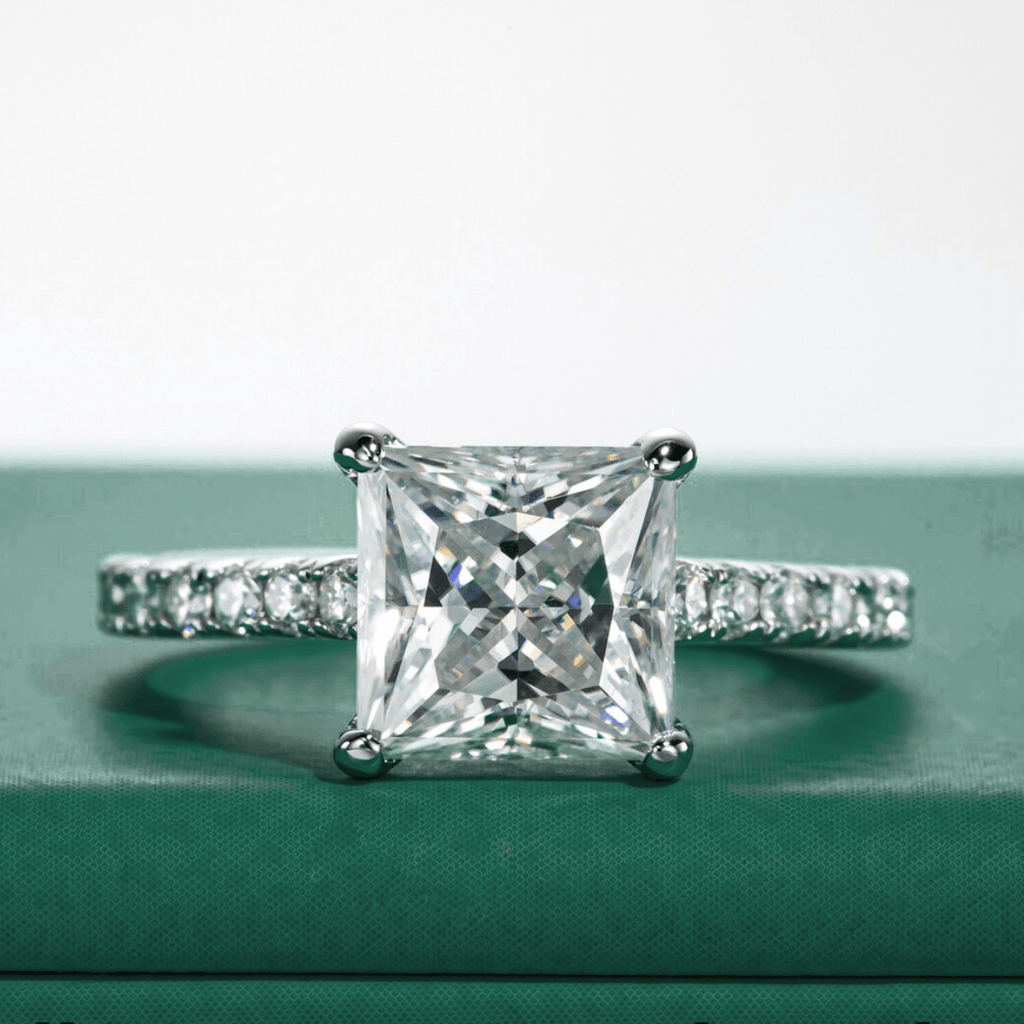 Anel solitário de moissanite princesa com pedras laterais cravejadas em fundo verde