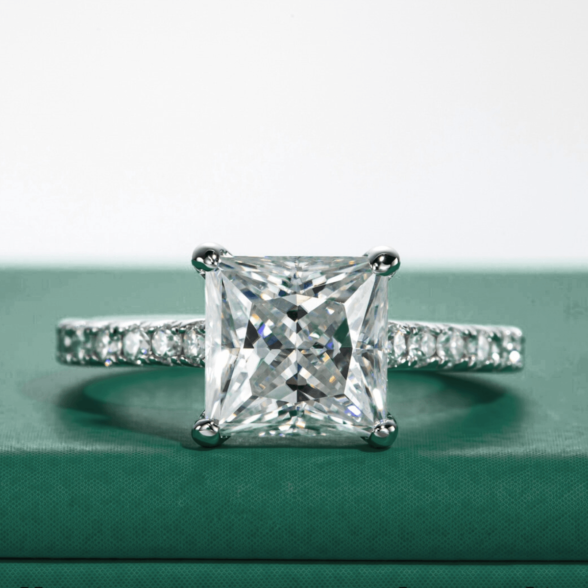 Anel solitário de moissanite princesa com pedras laterais cravejadas em fundo verde